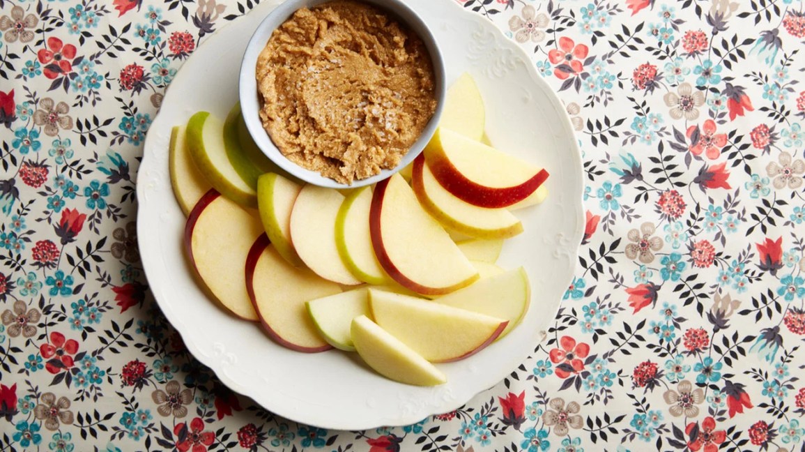 A plate of apple slices and cashew butter on a floral tablecloth.