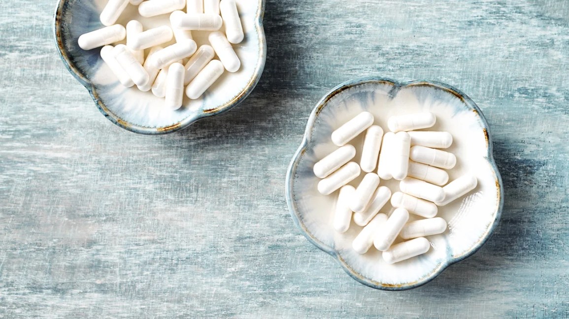 White supplement pills containing collagen in two small bowls on a blue table