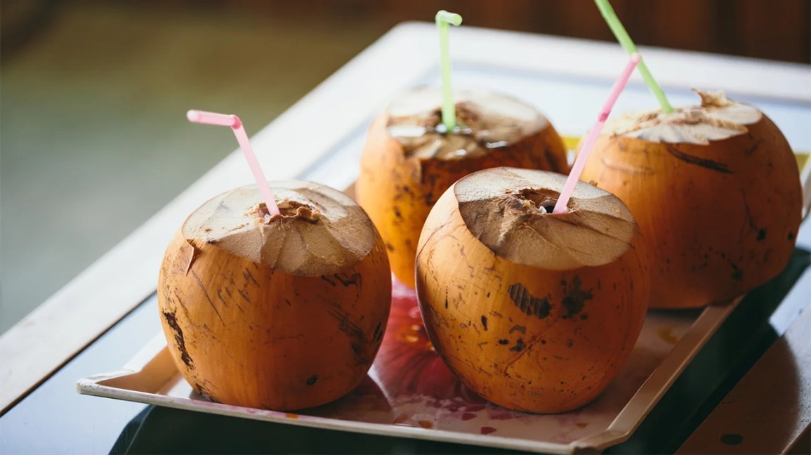 Four open coconuts with straws in them